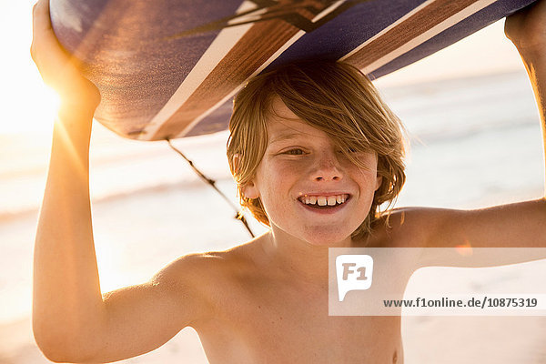 Boy carrying surfboard over head smiling