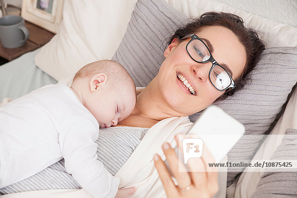 Baby boy sleeping on mother  mother using smartphone