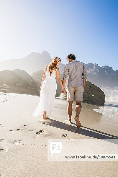 Full length rear view of couple walking on beach holding hands