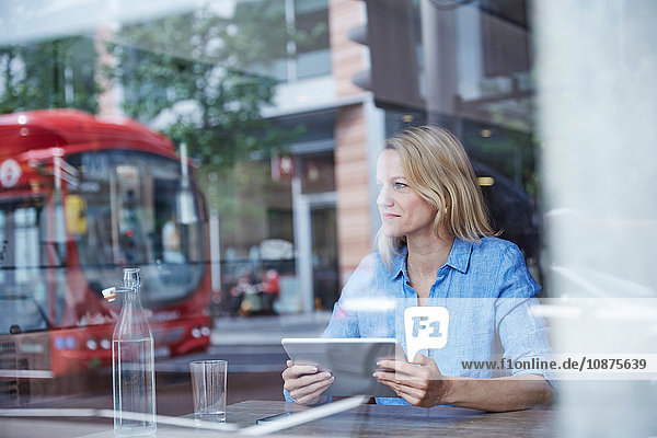 Reife Frau sitzt im Café  benutzt digitales Tablet  Bus spiegelt sich im Fenster