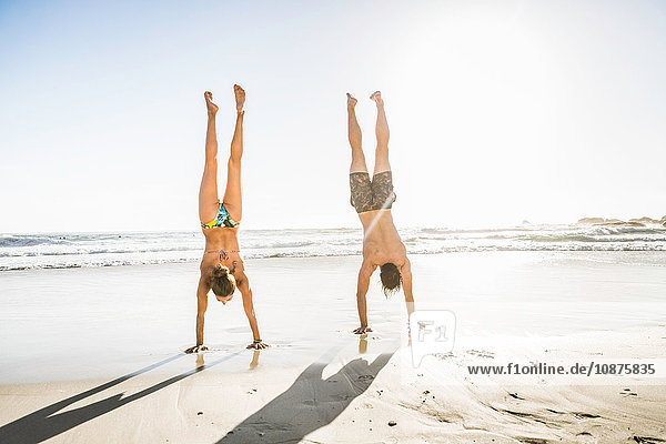 Mid adult couple doing handstands on beach Cape Town South Africa