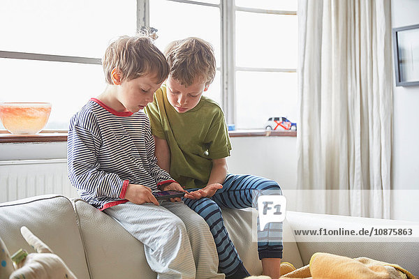 Boys wearing pyjamas sitting on sofa looking at smartphone