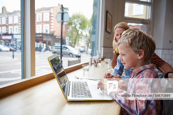 Mother and son at window seat in cafe using laptop