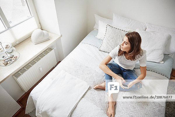 High level view of beautiful young woman sitting on bed gazing through window