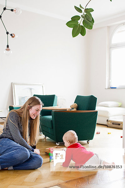 Mittelgroße erwachsene Frau und kleine Tochter spielen mit Bauklötzen auf dem Wohnzimmerboden