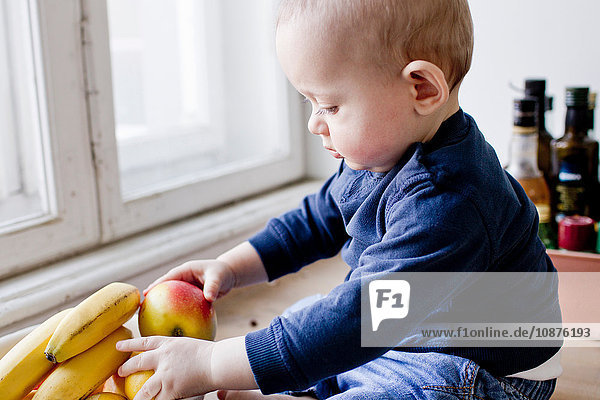 Kleiner Junge sitzt auf dem Küchentisch und spielt mit einer Obstschale