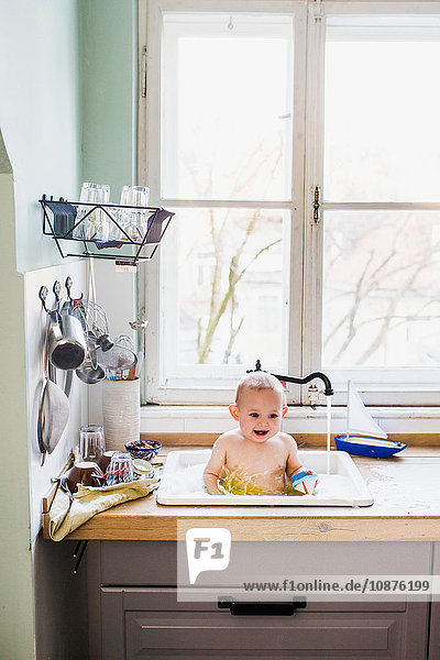 Porträt eines in der Küchenspüle badenden kleinen Jungen