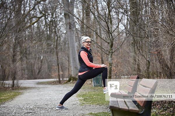 Reife Frau trainiert im Park  streckt die Beine auf der Parkbank