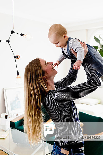 Woman holding up baby daughter in living room