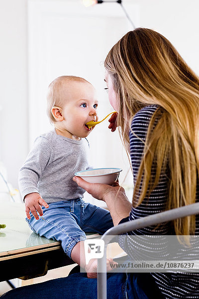 Mittlere erwachsene Frau  die ihre kleine Tochter auf dem Küchentisch füttert