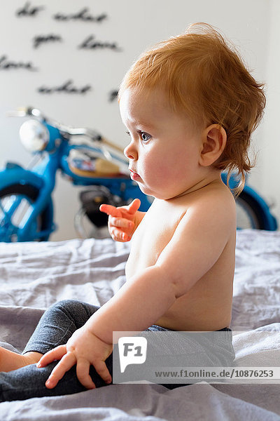 Auf dem Bett sitzendes Mädchen zeigt mit dem Finger auf das Bett