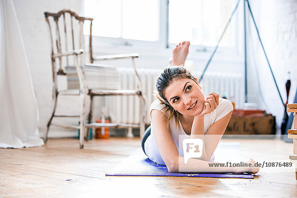 Porträt einer jungen Frau  die auf einer Yogamatte in der Wohnung liegt