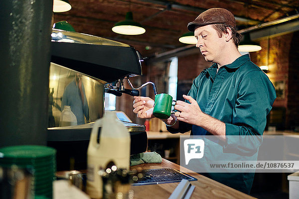 Männlicher Barista erhitzt Milchkännchen auf Kaffeemaschine im Café
