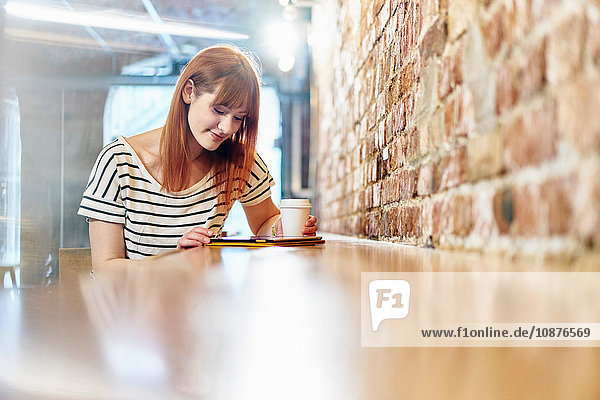 Weibliche Kundin sitzt auf Bank und blättert auf digitalem Tablet im Café