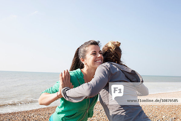 Zwei Frauen beim Aufwärmtraining  aneinander gelehnt am Strand von Brighton