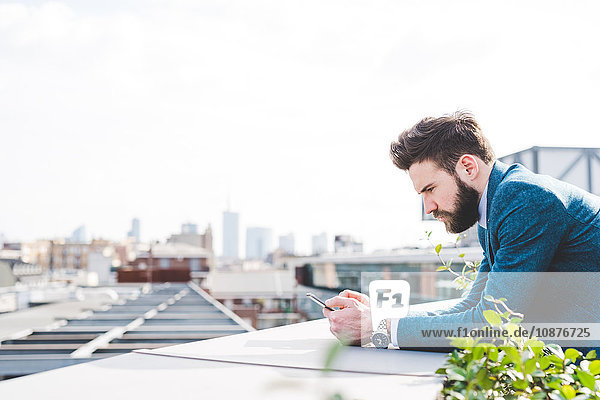 Junger Geschäftsmann liest Smartphone-Text auf Büro-Dachterrasse