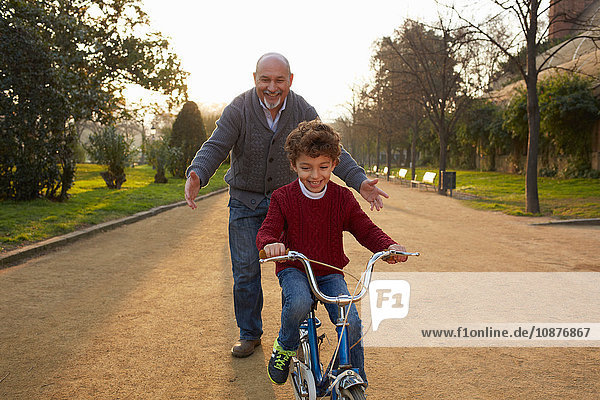 Grandfather teaching grandson to ride bicycle in park