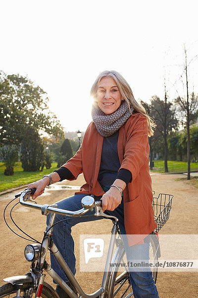 Reife Frau im Park auf dem Fahrrad  die lächelnd in die Kamera schaut