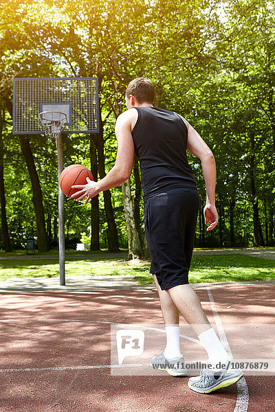 Rückansicht eines jungen männlichen Basketballspielers  der mit dem Ball auf dem Spielfeld läuft