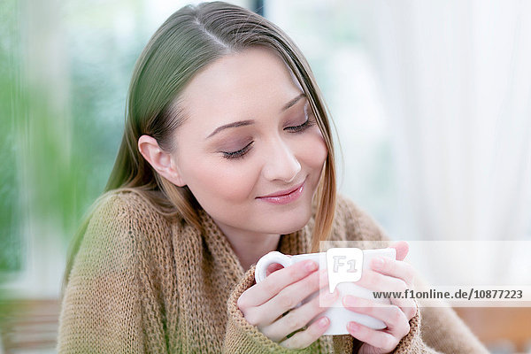 Frau hält Kaffeetasse mit geschlossenen Augen und lächelt