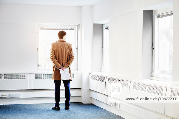 Rear view of man in empty office  hands behind back looking out of window
