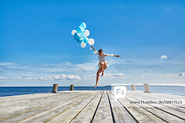 Junge Frau tanzt auf einem Holzsteg  hält einen Haufen Luftballons