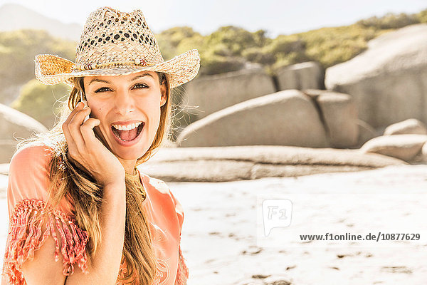 Porträt einer Frau mit Strohhut die sich mit einem Smartphone am Strand unterhält Kapstadt Südafrika