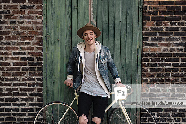 Porträt eines jungen Mannes  der sich an ein Fahrrad lehnt  im Freien