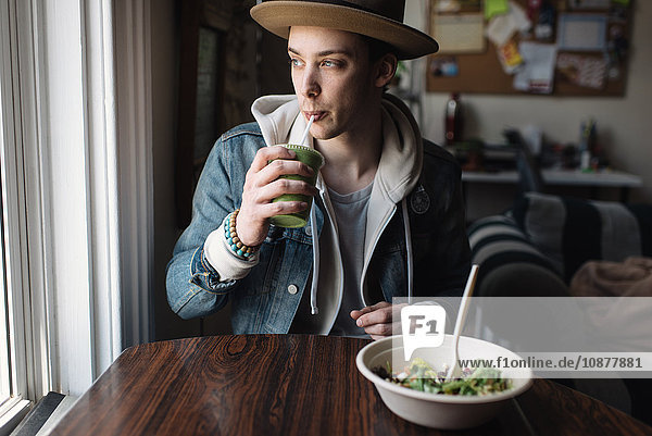 Junger Mann sitzt am Tisch  isst  trinkt Gesundheitsgetränk