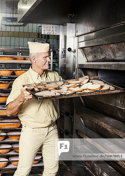 Fröhlicher Bäcker schiebt das Blech mit dem geschnittenen Brot in den Ofen