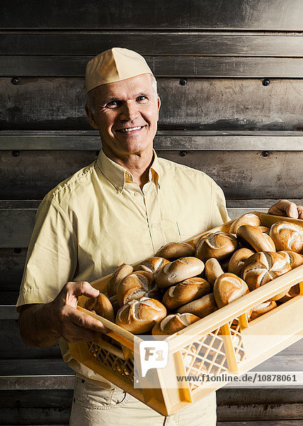 Happy baker carrying crate of bread rolls