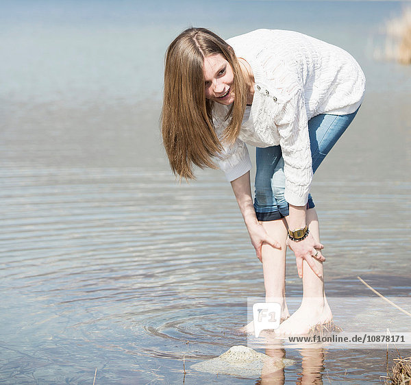 Teenager-Mädchen mit Jeans  die knöcheltief im Wasser zusammengerollt sind und sich nach vorne beugen