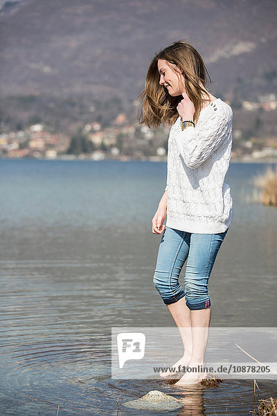 Seitenansicht eines Teenager-Mädchens mit knöcheltief zusammengerollter Jeans im Wasser