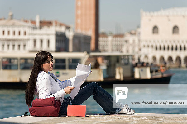 Junge Frau beim Kartenlesen am Wasser gegenüber dem Markusplatz,  Venedig,  Italien