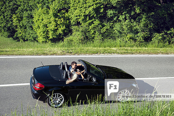 Älteres Paar im Cabriolet mit Smartphone zum Fotografieren