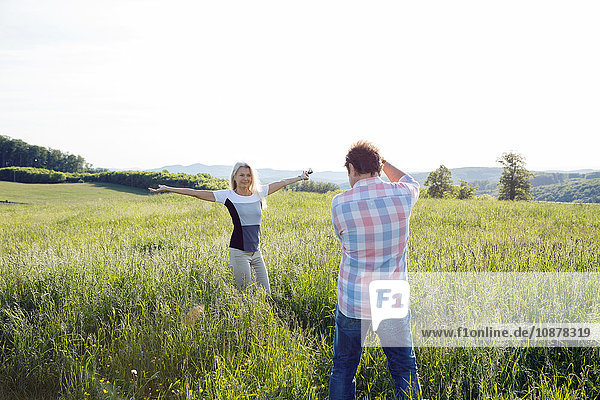 Man photographing woman in field