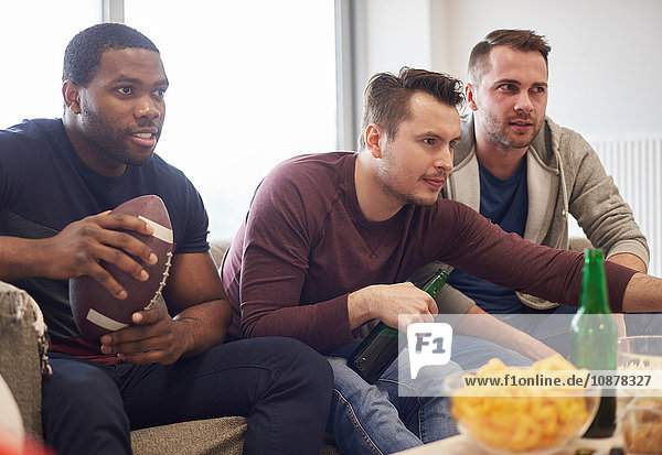 Group of men holding ball watching sports event on television with snacks and beers