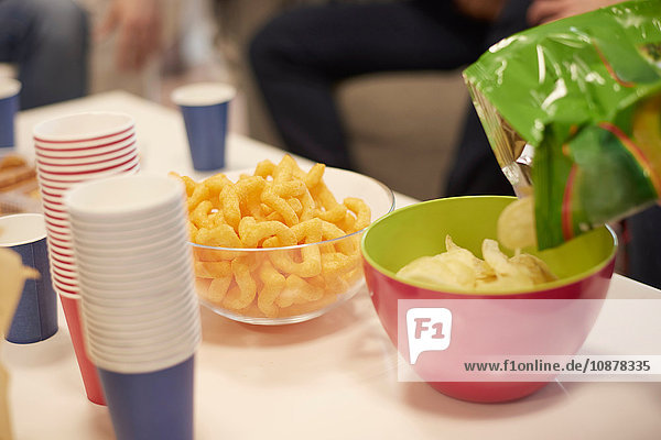 Cropped view of table with disposable cups and bowls of potato chips and snacks