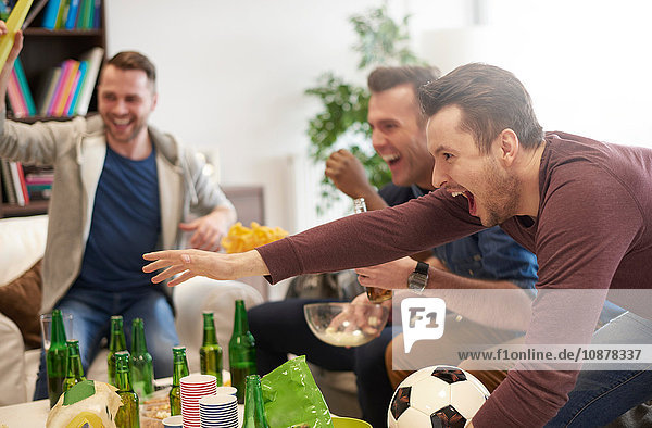 Group of men watching sporting event on television holding football celebrating