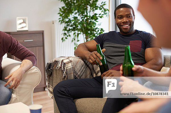 Gruppe von Männern sitzt im Salon und hält Bierflaschen lächelnd in der Hand
