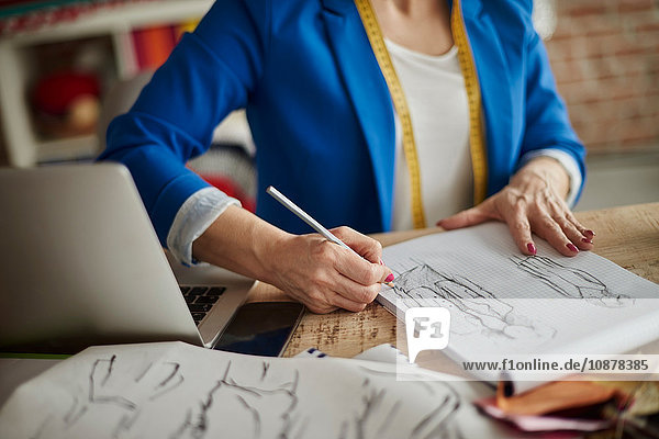 Ausschnitt einer Frau  die am Schreibtisch sitzt und Modedesign skizziert