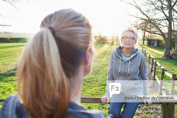 Women wearing sports clothing leaning against fence talking to friend