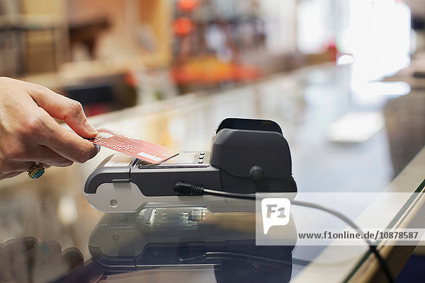 Schrägansicht der Hand einer Frau  die eine Kreditkarte benutzt  um kontaktlos an einem Chip- und Pin-Automaten zu bezahlen