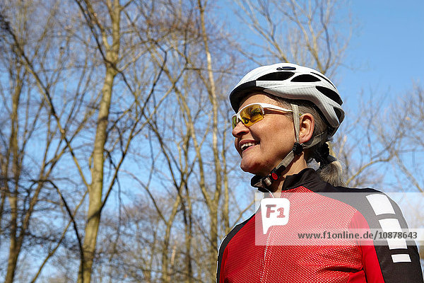 Niedriger Blickwinkel auf eine Frau mit Fahrradhelm und Sonnenbrille  die lächelnd wegschaut