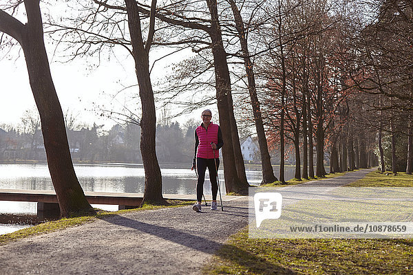 Nordic-Walking-Frau auf baumgesäumtem Weg am Teich