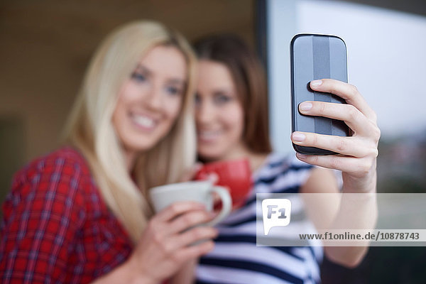 Two female friends  drinking coffee  outdoors  taking self portrait using smartphone