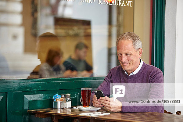 Reifer Mann liest Smartphone-Text am Tisch im Straßencafé