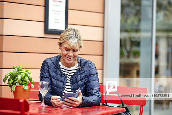 Reife Frau liest im Straßencafé Smartphone-Texte