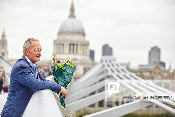 Reifer Mann mit Blumenstrauss wartet auf der Millennium Bridge  London  UK
