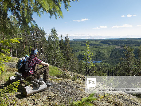 Schweden Medelpad Storberget naturreservat Wanderer auf Holzbank im Wald sitzend und mit Blick auf die Aussicht
